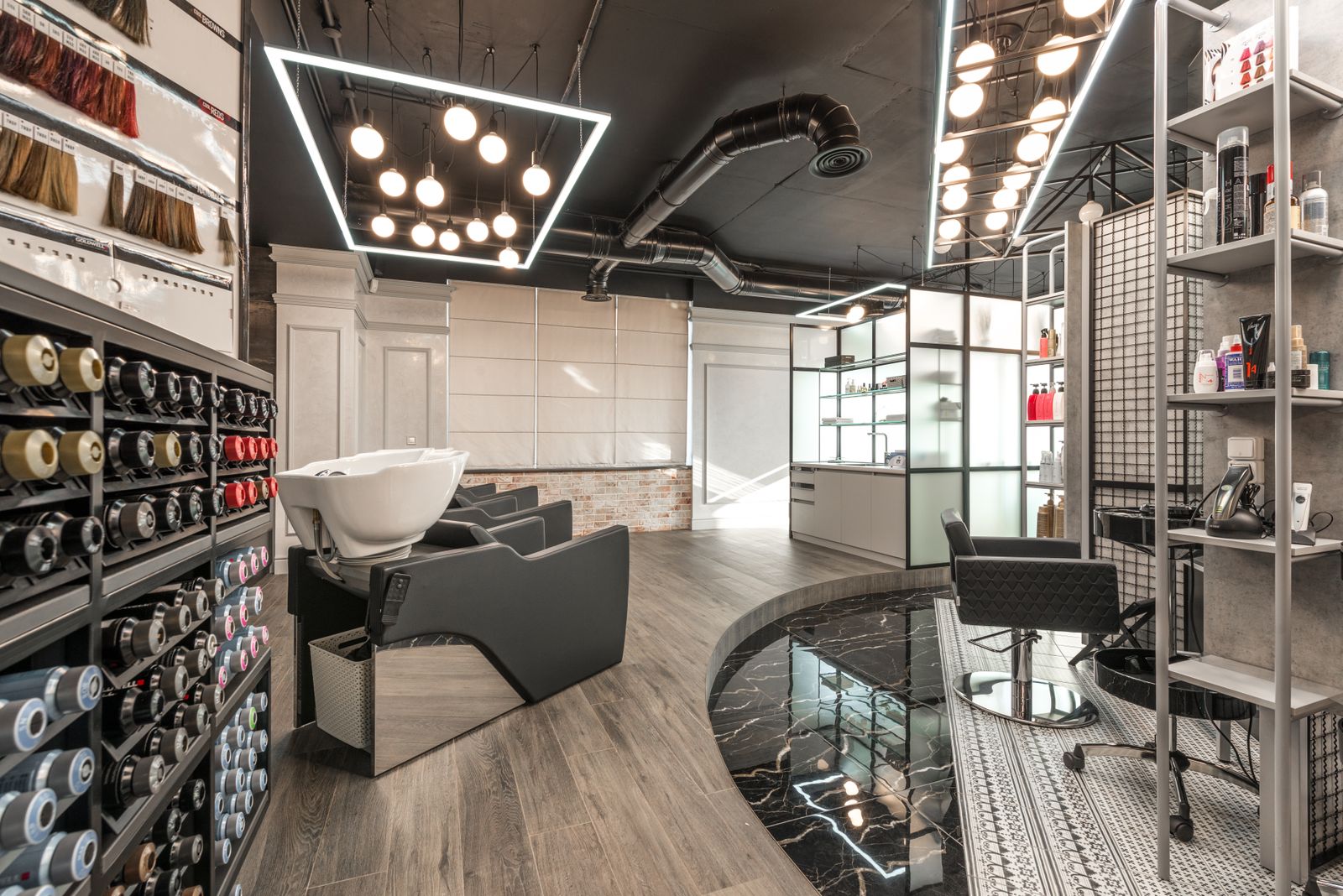 Black backwash chair with white sink placed in modern stylish beauty salon with various cosmetology products and bright glowing lamps